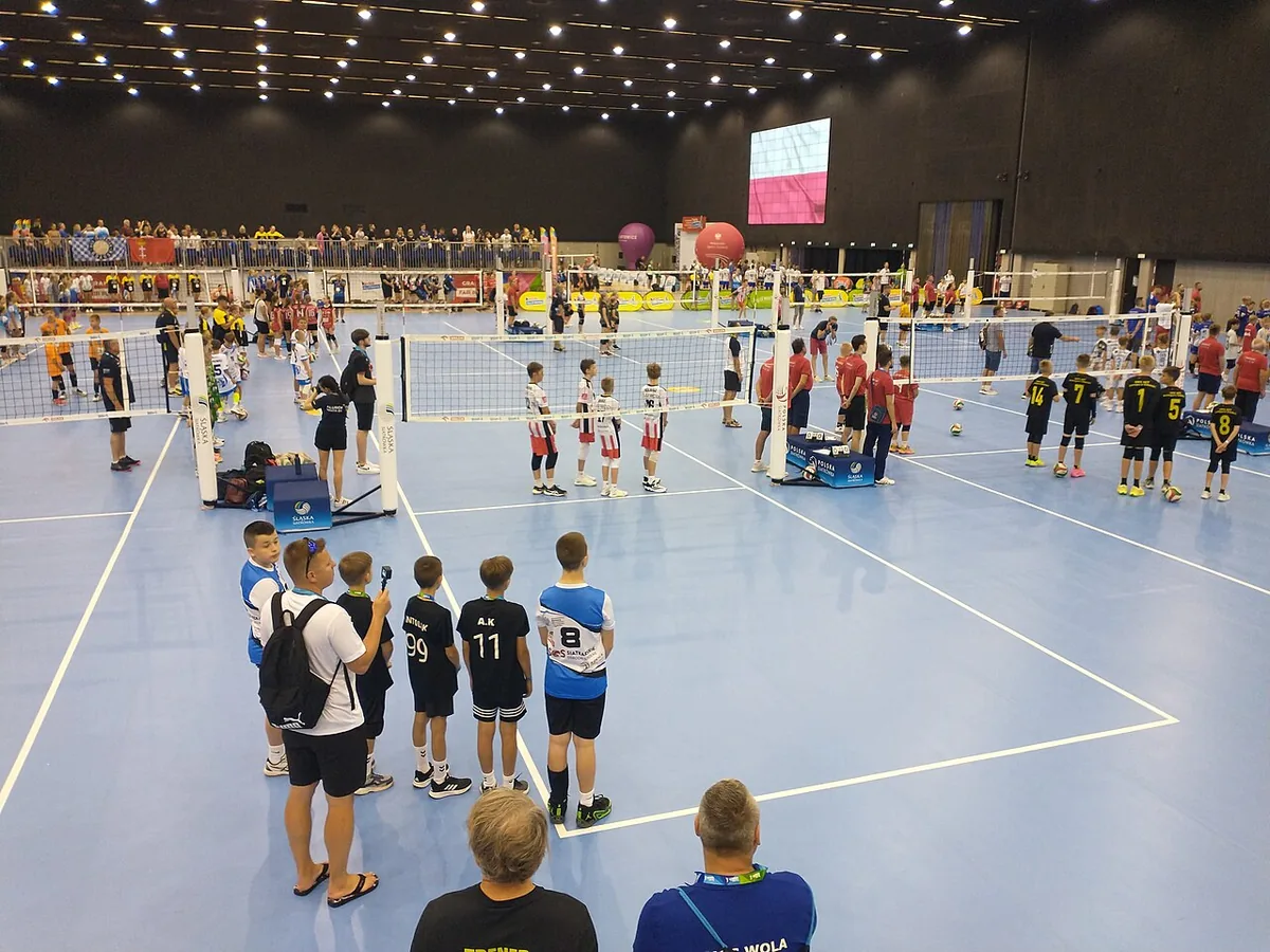Pabellón con varios campos de minivoley montados uno al lado de otro y equipos de niños de cuatro jugadores esperando para jugar