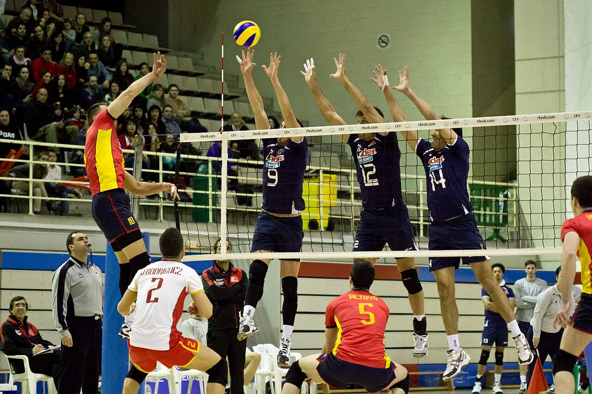 Un atacante de la selección española remata contra un triple bloqueo de Portugal mientras dos compañeros se agachan para cubrir