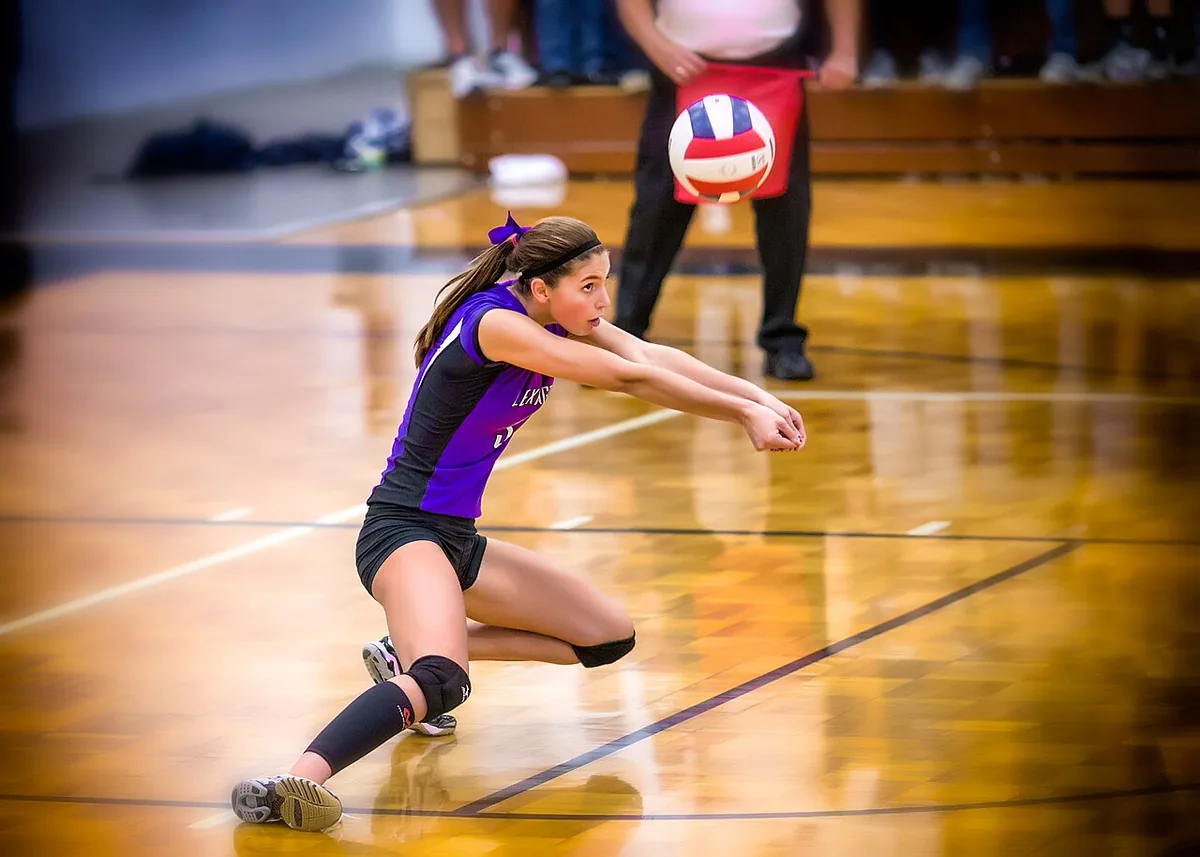Jugadora de voleibol con una rodilla casi en el suelo y los brazos estirados y unidos para jugar de antebrazo un balón bajo