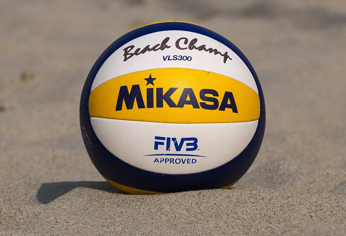 Balón Mikasa VLS300 Beach Champ blanco, amarillo y azul con el sello FIVB Approved, apoyado en la arena